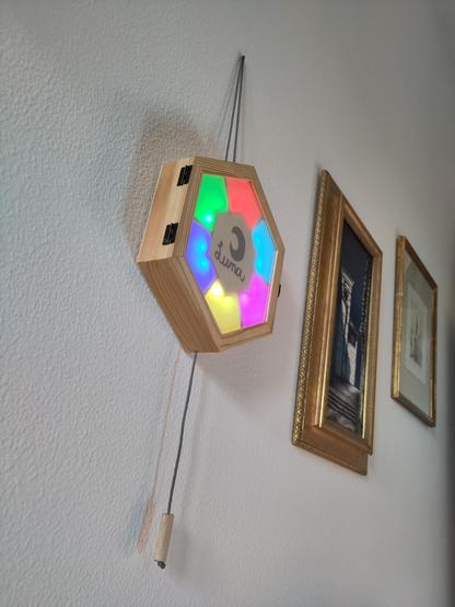 A colorful game for babies. It's an hexagonal wooden box with an hexagonal plexiglass window divided in 6 sections, every sections lit with a different colour. A cord comes out from the bottom and terminates in a wooden handle. A piece of rope allows it to be hung.