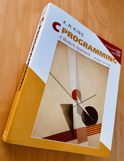 The book "C Programming, A modern Approach" by K.N. King. The cover shows an abstract art piece with geometric shapes.
