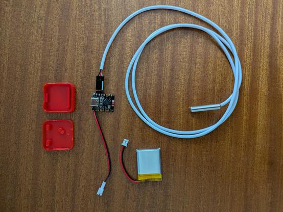 A thumbnail-sized ESP32 SOC with temperature probe and a LiPo battery, and a 3D printed case sitting next to it.