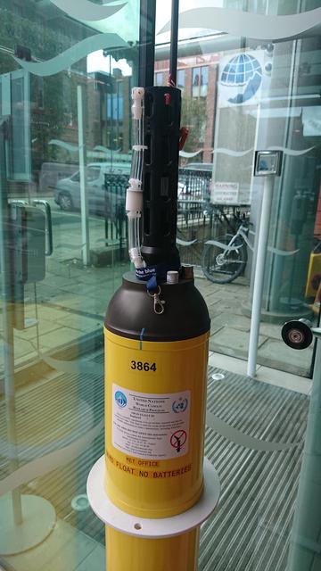A tall thin metal cylinder, painted yellow, with a protrusion of sensors poking out of the top