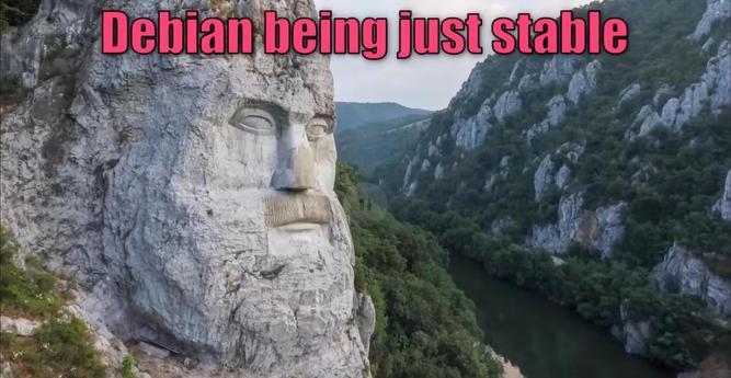 Stone face sculpture carved into a mountainside, overlooking a river valley. Text at the top reads "Debian being just stable" in pink font. The scene conveys grandeur and stability.
