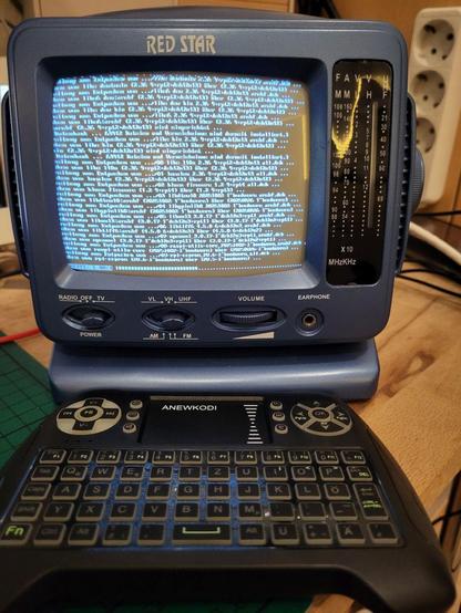 Kleiner Röhren-Schwarzweiß-Fernseher mit zeilenweise Text auf dem Bildschirm. Davor eine kleine drahtlose Tastatur mit Gummitasten.