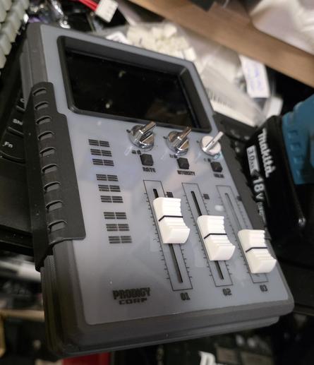 A replica of the hybrid control device from Alien Earth. It is a rectangular gray device with three faders, three buttons, three knobs, and a screen at the top