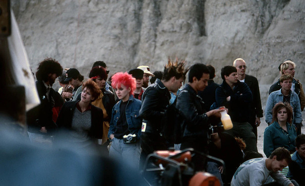 A color photo of punks having just arrived in the desert gathering to watch the event. In the background you can see the cliff face.