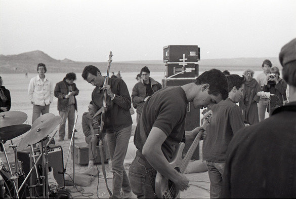 A black-and-white photo of Savage Republic performing live in the desert. In the background you can see a playa and hills in the distance.