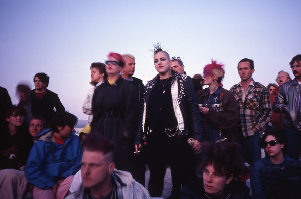 A color photo of punks hanging out in the desert, watching the show.