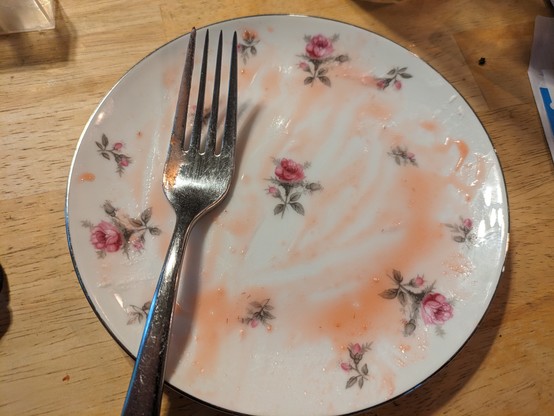 A fork rests on an empty plate. Some of the juice that couldn't be mopped or licked is visible. 

The roses from the design of plate are visible