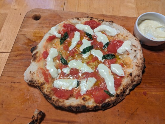Margherita pizza with a small cup of garlic cream sauce next to it