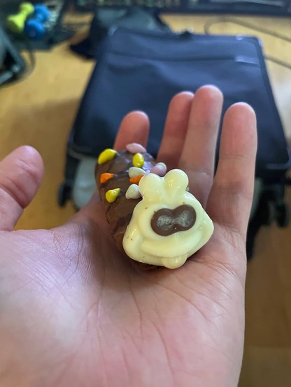 A Colin the Caterpillar mini roll, held in a hand in front of a suitcase