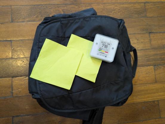 Two vibrant green-yellow napkins with an Aranet4 C02 device at 718 parts per million on a black shoulder bag. It's all coincidentally arranged like the LGM logo.with three squarish rectangles.