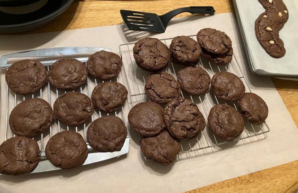 A couple dozen Nutella cookies cooling on racks. In the background a cookie sheet is visible with something on it…
