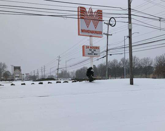 An accretion of sleet and ice coats the ground in Memphis, Tennessee, January 26, 2026. Here at the intersection of Germantown Parkway and Macon Road in Cordova, the Whataburger sign stands out with its signature orange against whited-out pavement. "24 hours," it says, but not this day.