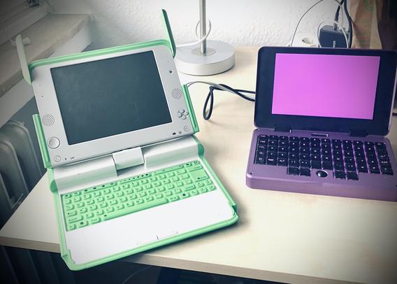 A greeen OLPC XO-1 and a purple MNT Pocket Reform on a desk.