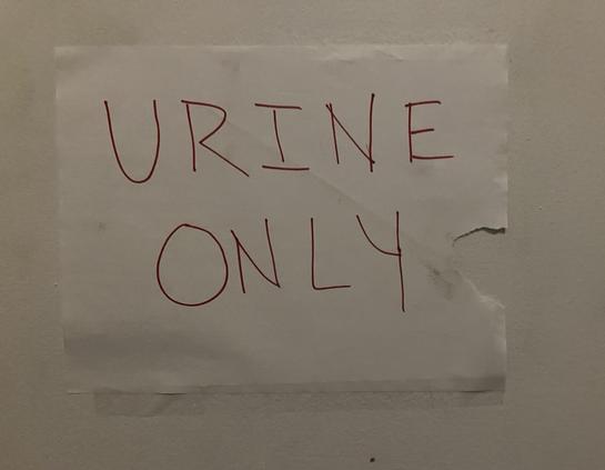 A piece of paper with “URINE ONLY” written on it in red ink. The paper is taped to the wall of a bathroom stall above the toilet, inside a church in Memphis, Tennessee