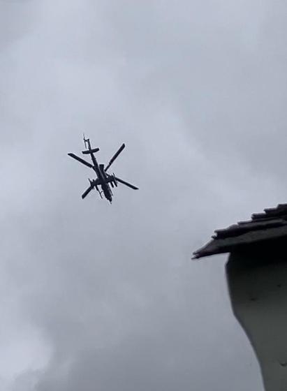 An AH-64 Apache attack helicopter flies over my house like an angry mosquito. The sky is gray with clouds. A corner of my roof juts into the photo from the lower right. Memphis, Tennessee, April 29 2026.