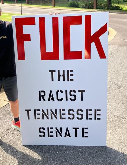 A protestor stands next to his very large sign which says “FUCK the racist Tennessee senate.” The word “FUCK” is very big in red block letters; the remainder is in smaller black stenciled letters. The sign is almost as tall as the man. Memphis, Tennessee, May 15, 2026.