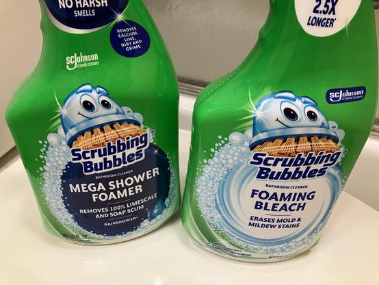 A bottle of Scrubbing Bubbles Mega Shower Foamer (no bleach, mostly lactic acid) next to a bottle of Scrubbing Bubbles Foaming Bleach (contains bleach). Both bottles are the same hue of green, with minor differences in the product logo.