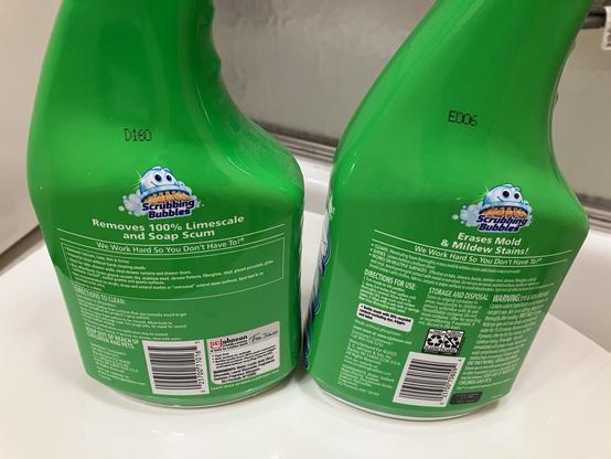 A bottle of Scrubbing Bubbles Mega Shower Foamer (no bleach, mostly lactic acid) next to a bottle of Scrubbing Bubbles Foaming Bleach (contains bleach). Both bottles are the same hue of green. Here, the backs of the bottles are shown; they’re almost indistinguishable from one another 