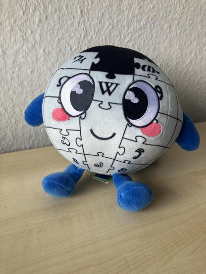 Baby Globe, a cuddly mascot celebrating Wikipedia’s 25th birthday. The plushie is a friend-shaped iconic puzzle-piece globe with sparkling eyes, rosy cheeks, and bright blue arms and feet. Baby Globe serves as a cute representation of "a world in which every human being can freely take part in the sharing of all knowledge" (Jimmy Wales).