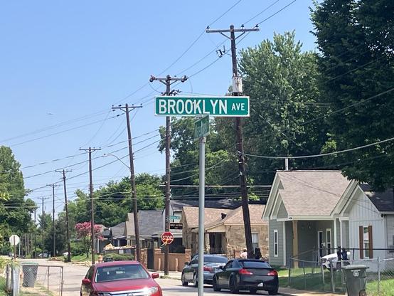 The intersection of Brooklyn Avenue and Marechalneil Street in historic Orange Mound, Memphis, Tennessee. A residential street with homes and cars takes up most of the frame. The focus of the photo is the street sign, looking at the “Brooklyn Ave” side.