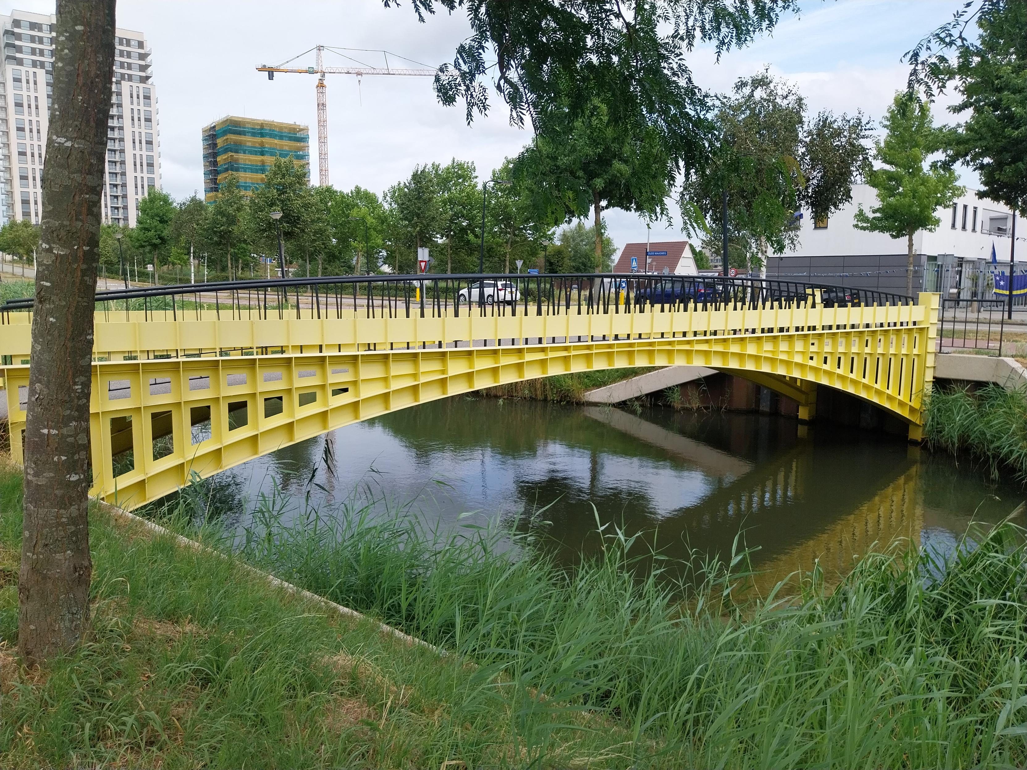 A small, yellow bridge crossing a waterway. The bridge is designed to look like the bridge on a 50 euro note.