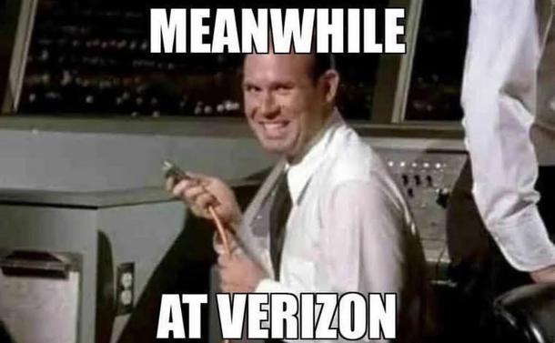 A man is seated at a console. He’s holding an unplugged power cord and grinning. A meme caption says “Meanwhile at Verizon”