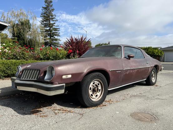THIS is a 1975 Chevy Camaro with an inline six-cylinder engine and a floor-mounted three-speed manual transmission. The rust colored paint job has a uniquely aged patina. Parts of this beast are held together with actual duct tape and cobwebs.