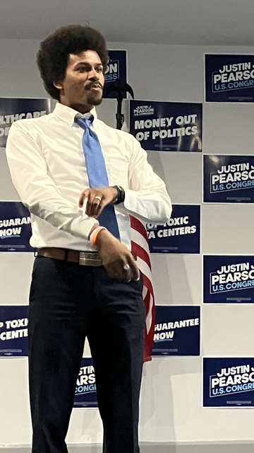 Tennessee state Representative Justin J. Pearson stands on the dais at his Memphis, Tennessee campaign headquarters, September 2nd, 2026. Behind him, small campaign signs are arranged in a checkerboard pattern on the wall.