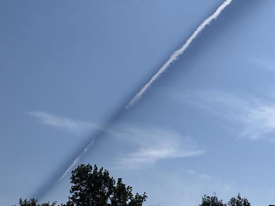A contrail angles across the sky toward the horizon, giving the impression that it hits the ground in the distance. The bright sun is casting an intense shadow behind the contrail. Memphis, Tennessee, September 20, 2026