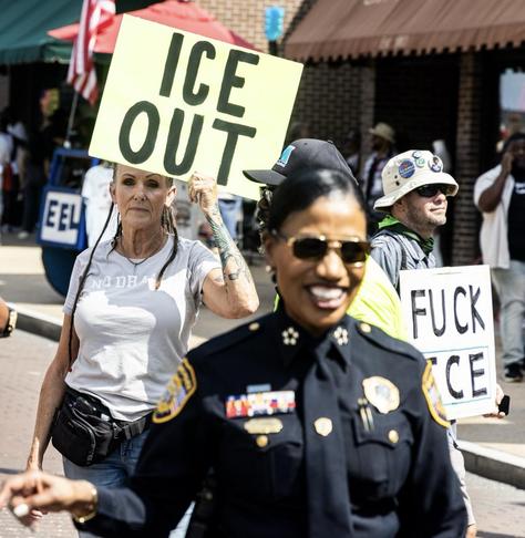 Memphis police chief CJ Davis strolls down Beale Street in Memphis, Tennessee. She’s bearing a big smile as she does a meet-and-greet with 901 Day celebrants. Behind her, two activists are holding signs, one that says ICE OUT and one that says FUCK ICE. Davis and her boss, Memphis mayor Paul Young, have been cooperating with ICE despite repeated denials. Photo courtesy Daily Memphian.